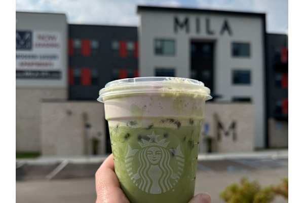 A hand is holding a Starbucks drink in front of a building.